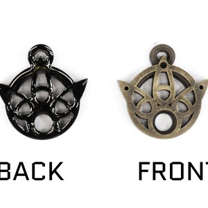 May include: A black metal pendant with an intricate design, showing the front and back sides. The pendant has a circular shape with a hole in the center and a small loop at the top for attaching a chain.