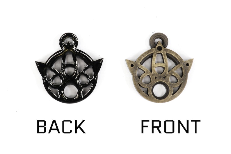 May include: A black metal pendant with an intricate design, showing the front and back sides. The pendant has a circular shape with a hole in the center and a small loop at the top for attaching a chain.