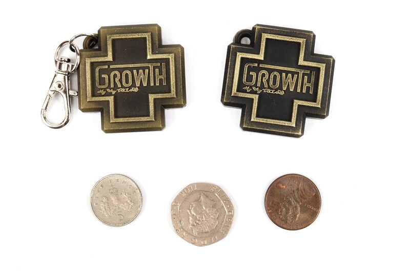 May include: Two gold-colored metal keychains with the word "GROWTH" on them. The keychains are in the shape of a cross. There are three coins below the keychains, two silver and one copper.