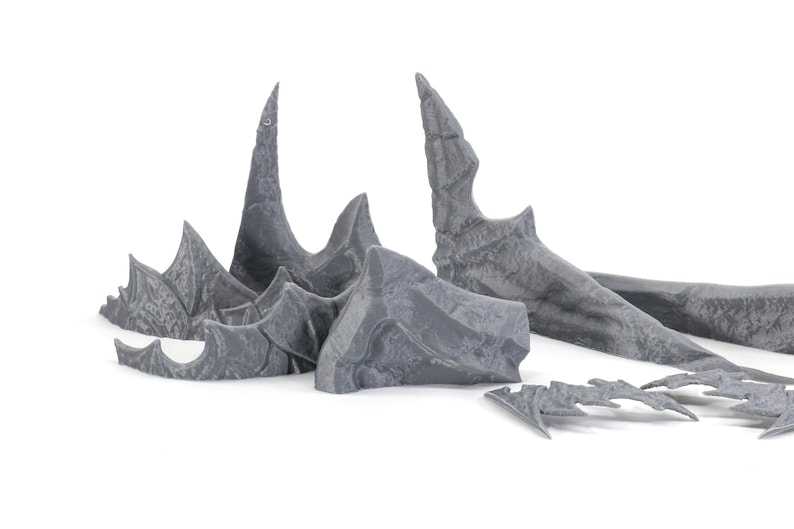 May include: A set of grey plastic dragon wings for a miniature figure. The wings are detailed with textured scales and sharp points.