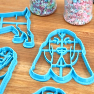 May include: A set of four blue plastic cookie cutters shaped like dogs. The cutters are on a wooden surface.