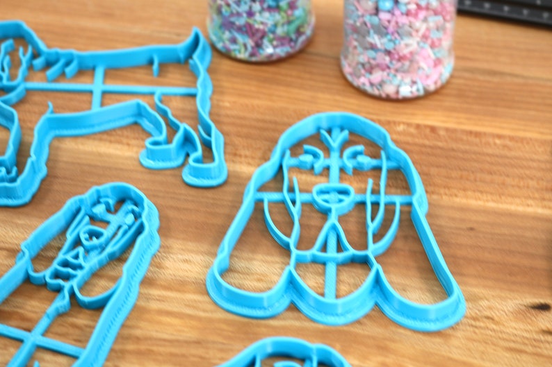May include: A set of four blue plastic cookie cutters shaped like dogs. The cutters are on a wooden surface.