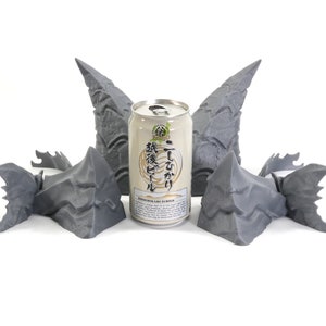Op de afbeelding: Vijf 3D-geprinte grijze drakenkop-sculpturen rond een blikje Japans bier. Het blikje heeft Japanse tekst en de woorden "Japanese Craft Beer" erop gedrukt.