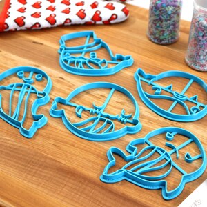 Peut inclure: Un ensemble de cinq emporte-pi&egrave;ces en plastique bleu en forme de pingouins. Les emporte-pi&egrave;ces sont sur une surface en bois avec des p&eacute;pites dans des bocaux et un rouleau &agrave; p&acirc;tisserie.