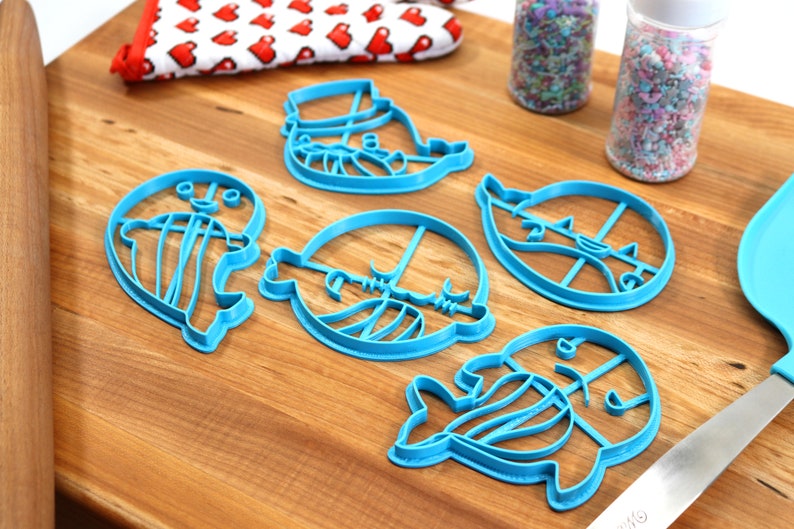 Peut inclure: Un ensemble de cinq emporte-pi&egrave;ces en plastique bleu en forme de pingouins. Les emporte-pi&egrave;ces sont sur une surface en bois avec des p&eacute;pites dans des bocaux et un rouleau &agrave; p&acirc;tisserie.