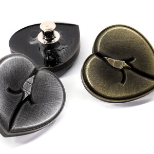 May include: Three heart-shaped metal buttons with a broken heart design. Two buttons are silver and one is gold.