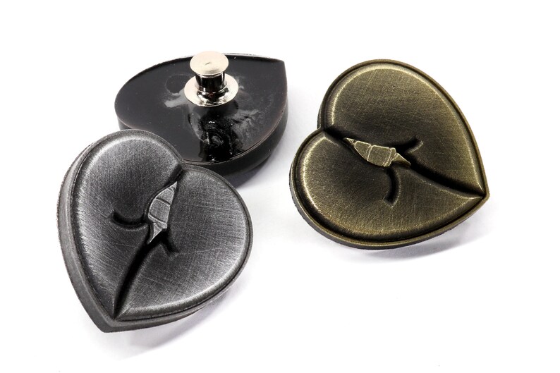 May include: Three heart-shaped metal buttons with a broken heart design. Two buttons are silver and one is gold.