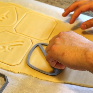 May include: A person using a cookie cutter to cut out shapes from a sheet of cookie dough. The cookie cutter is shaped like a peace sign.