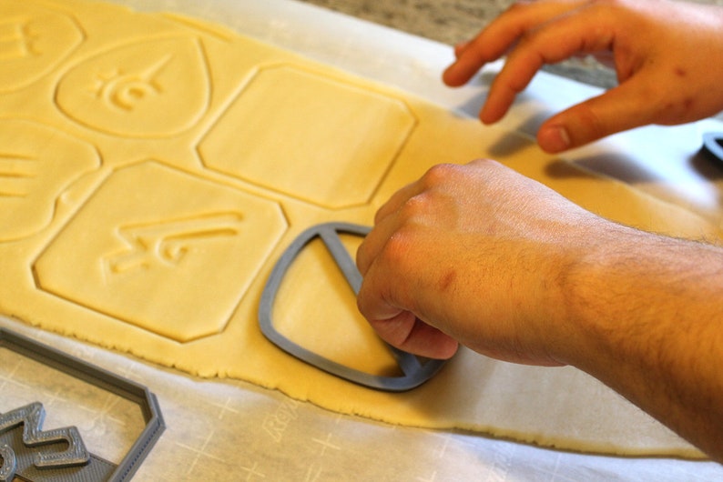 May include: A person using a cookie cutter to cut out shapes from a sheet of cookie dough. The cookie cutter is shaped like a peace sign.