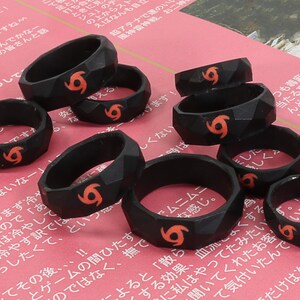 May include: A set of eight black silicone rings with a raised, textured design. Each ring features a red, stylized tornado symbol.