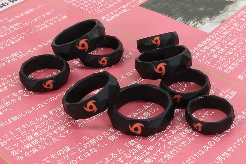 May include: A set of eight black silicone rings with a raised, textured design. Each ring features a red, stylized tornado symbol.