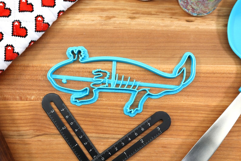 May include: A blue plastic cookie cutter shaped like an axolotl. The axolotl is a type of salamander that is native to Mexico.