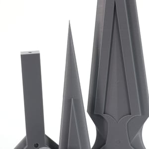 May include: Three gray 3D printed objects, a tall pointed shape, a shorter cone shape, and a rectangular shape with a pointed top.