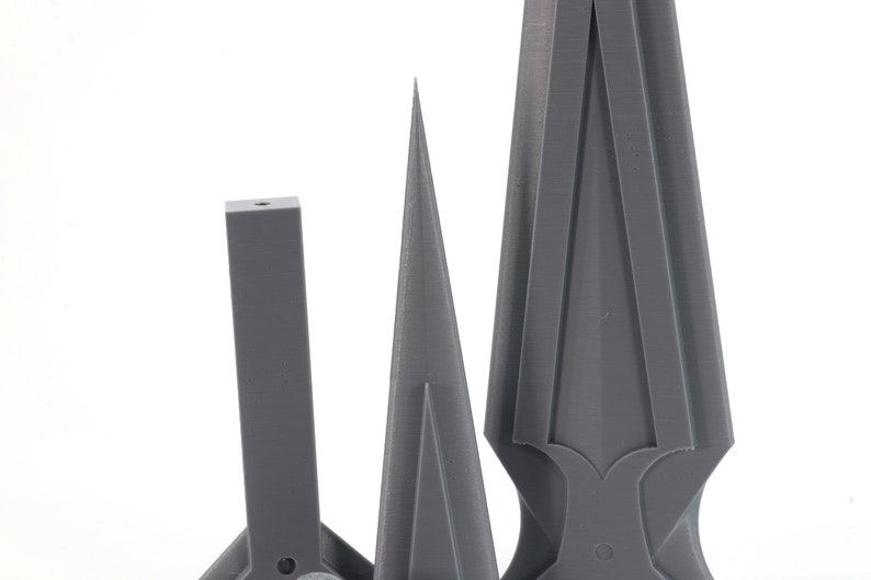 May include: Three gray 3D printed objects, a tall pointed shape, a shorter cone shape, and a rectangular shape with a pointed top.