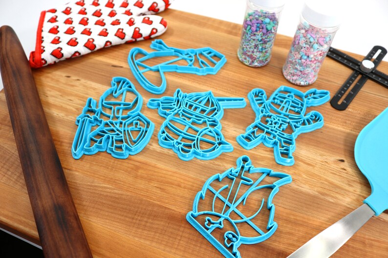 May include: A set of blue plastic cookie cutters shaped like knights and a ship. The cutters are on a wooden surface with sprinkles in jars and a rolling pin.
