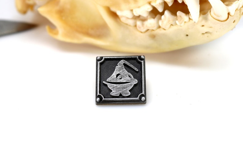 May include: A silver metal pin with a black background. The pin features a stylized image of a censer, a container used to burn incense.
