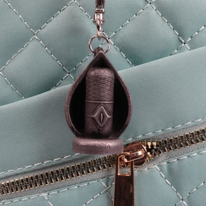 May include: A black metal microphone keychain with a silver ring. The keychain is attached to a light blue quilted bag with a gold zipper.