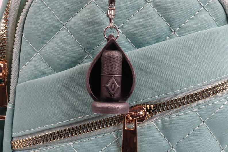 May include: A black metal microphone keychain with a silver ring. The keychain is attached to a light blue quilted bag with a gold zipper.