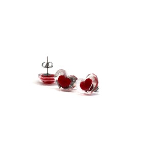 Puede incluir: Un par de pendientes transparentes en forma de coraz&oacute;n con corazones rojos en su interior. Los pendientes tienen postes de plata.