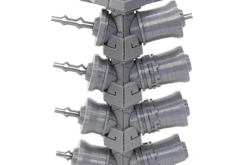 May include: A close-up of a gray 3D printed model of a tower with multiple cannons. The cannons are arranged in a vertical stack and have a detailed design.