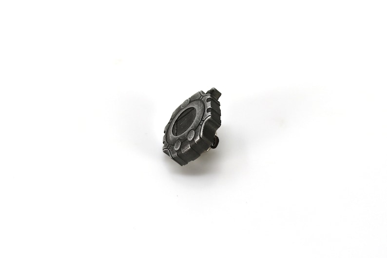 May include: A silver-colored metal pin shaped like a digital pet device. The pin has a black screen and a few buttons.
