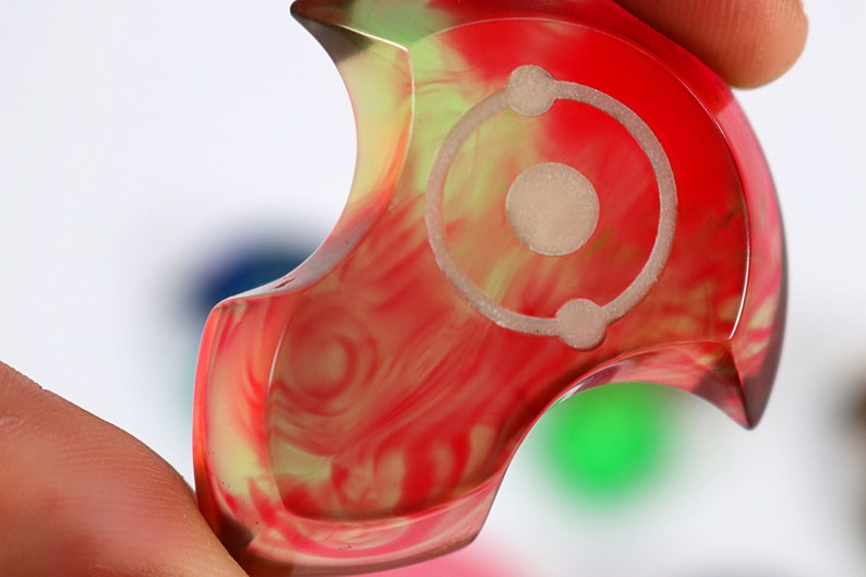 May include: A red, green and yellow swirl resin dice with a white circle and three dots in the centre.