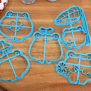 May include: Set of five blue plastic frog-shaped cookie cutters. The cutters feature different designs, including a frog with a mushroom, a frog with a leaf, and a frog with a flower.