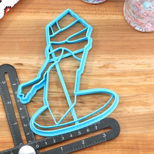 May include: A blue plastic cookie cutter shaped like a snowman wearing a hat and scarf. The cutter is on a wooden surface.