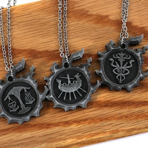 May include: Three silver necklaces with pendants featuring intricate designs. The pendants are circular and have a textured, aged look. Each pendant features a different design, including a ship, a scale, and a stylized flower.