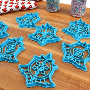 May include: Seven blue plastic cookie cutters shaped like stars with different designs inside each star. The cookie cutters are on a wooden surface.