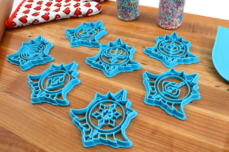 May include: Seven blue plastic cookie cutters shaped like stars with different designs inside each star. The cookie cutters are on a wooden surface.