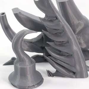 May include: A 3D printed gray plastic model of a pirate's hook, with a sharp point and a curved handle. The hook is part of a larger model, which is also visible in the image.