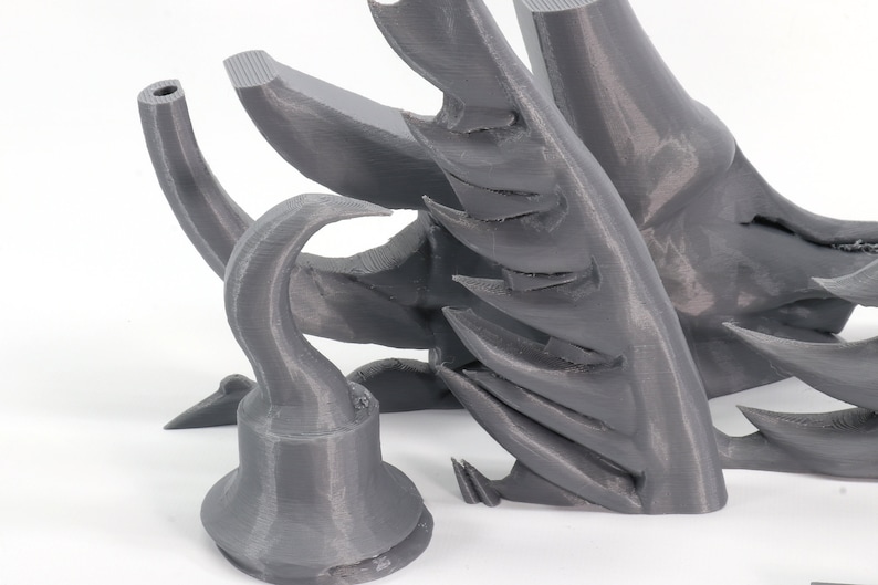 May include: A 3D printed gray plastic model of a pirate's hook, with a sharp point and a curved handle. The hook is part of a larger model, which is also visible in the image.