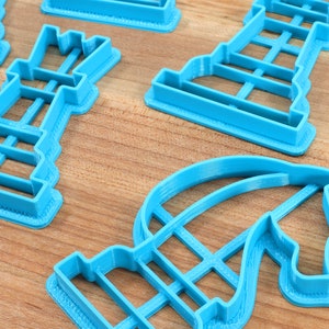 May include: A set of blue plastic cookie cutters shaped like chess pieces. The cutters are on a wooden surface.