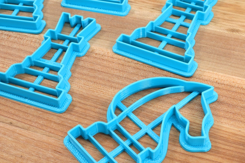 May include: A set of blue plastic cookie cutters shaped like chess pieces. The cutters are on a wooden surface.