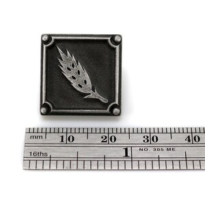 May include: A silver-toned metal square pin with a wheat stalk design. The pin is about 1 inch wide and is shown next to a ruler.