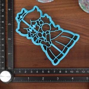 May include: Blue plastic cookie cutter shaped like a princess with a crown, holding a flower.