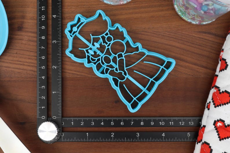 May include: Blue plastic cookie cutter shaped like a princess with a crown, holding a flower.