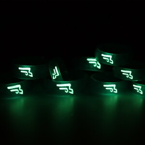 May include: A stack of glow-in-the-dark silicone bracelets with a white symbol on each. The symbol is a stylized letter "F" with wings.