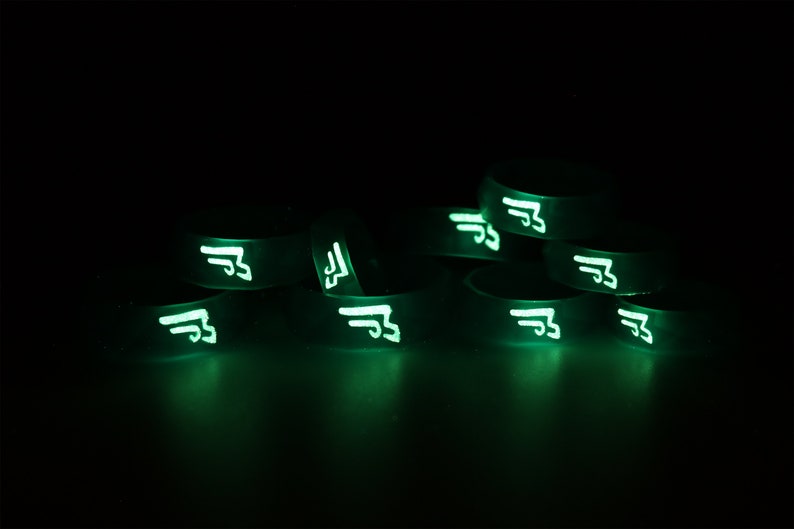 May include: A stack of glow-in-the-dark silicone bracelets with a white symbol on each. The symbol is a stylized letter "F" with wings.