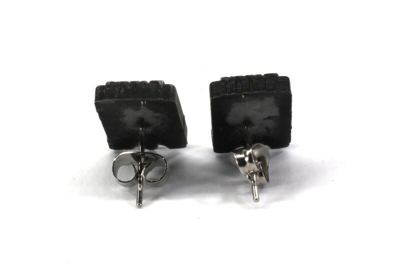May include: A pair of black square stud earrings with silver posts and backs.