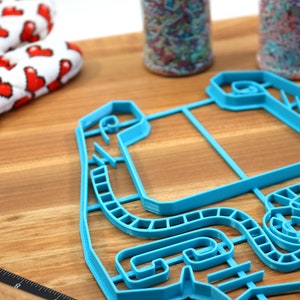 Peut inclure: Un emporte-pi&egrave;ce en plastique bleu en forme de circuit de course. L'emporte-pi&egrave;ce est sur une surface en bois.