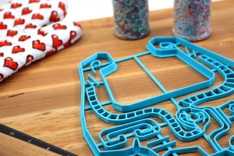 Peut inclure: Un emporte-pi&egrave;ce en plastique bleu en forme de circuit de course. L'emporte-pi&egrave;ce est sur une surface en bois.