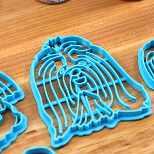 May include: Three blue plastic cookie cutters shaped like dogs. The cutters are on a wooden surface.