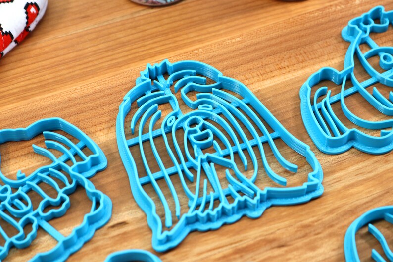 May include: Three blue plastic cookie cutters shaped like dogs. The cutters are on a wooden surface.