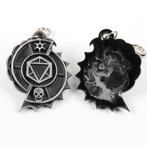 May include: Two silver metal keychains. One keychain features a circular design with a skull, a die, and a star. The other keychain is black and features a skull design.