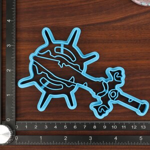 Puede incluir: Un cortador de galletas de pl&aacute;stico azul con forma de espada y rueda. El cortador mide aproximadamente 15 cm de largo y 10 cm de ancho.