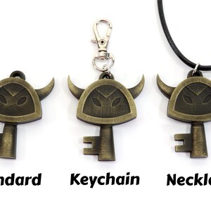 May include: Three versions of a gold-colored key pendant with a horned helmet design. The pendant is available as a standard charm, a keychain, and a necklace.