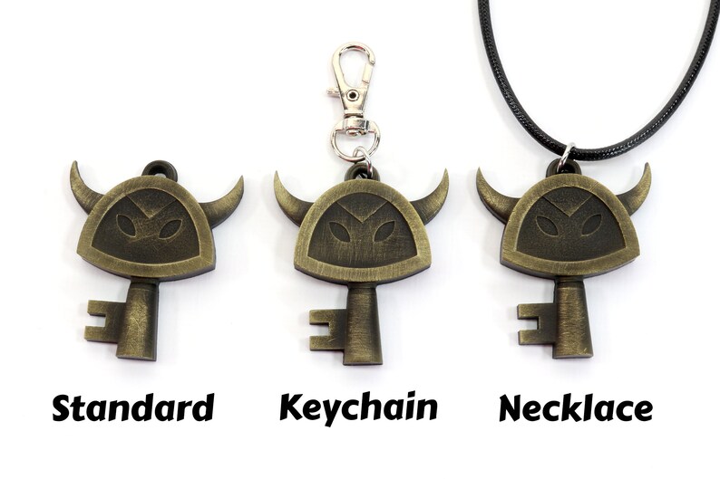 May include: Three versions of a gold-colored key pendant with a horned helmet design. The pendant is available as a standard charm, a keychain, and a necklace.