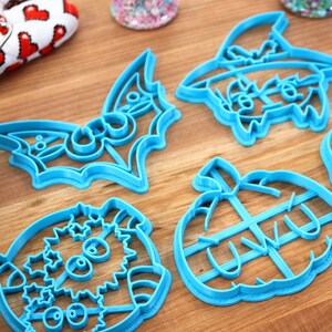 May include: A set of six blue plastic Halloween cookie cutters. The cutters are shaped like a bat, a pumpkin, a ghost, a skull, a witch, and a monster.
